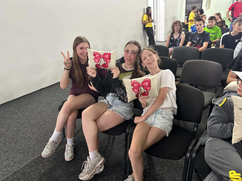 Three girls smiling and holding decorative cushions they made during the teenage summer camp.