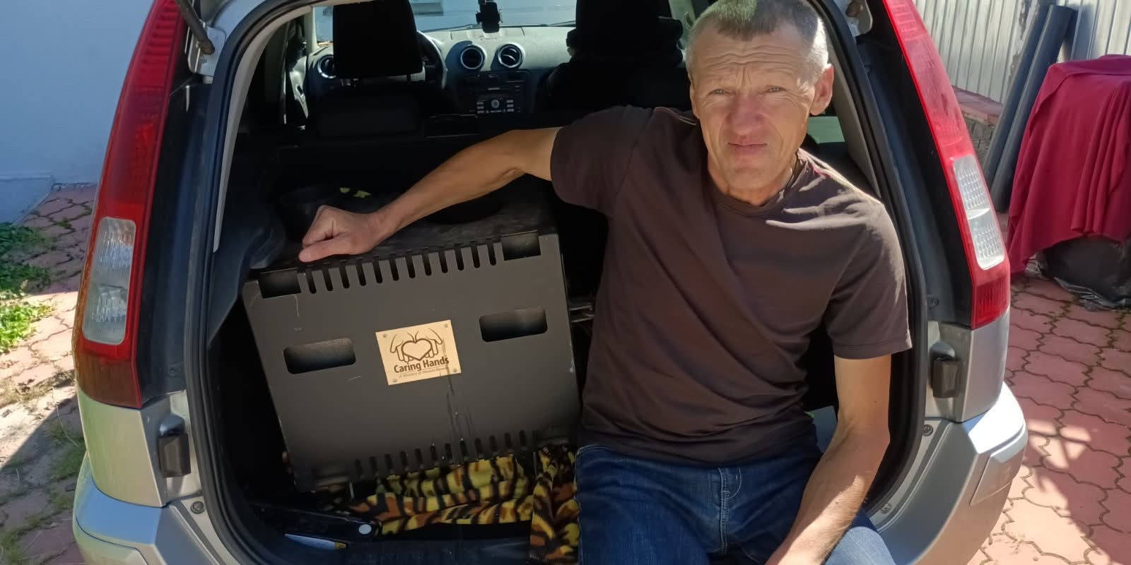 Man sitting beside a Caring Hands aid container in the boot of a car in Lebedyn.