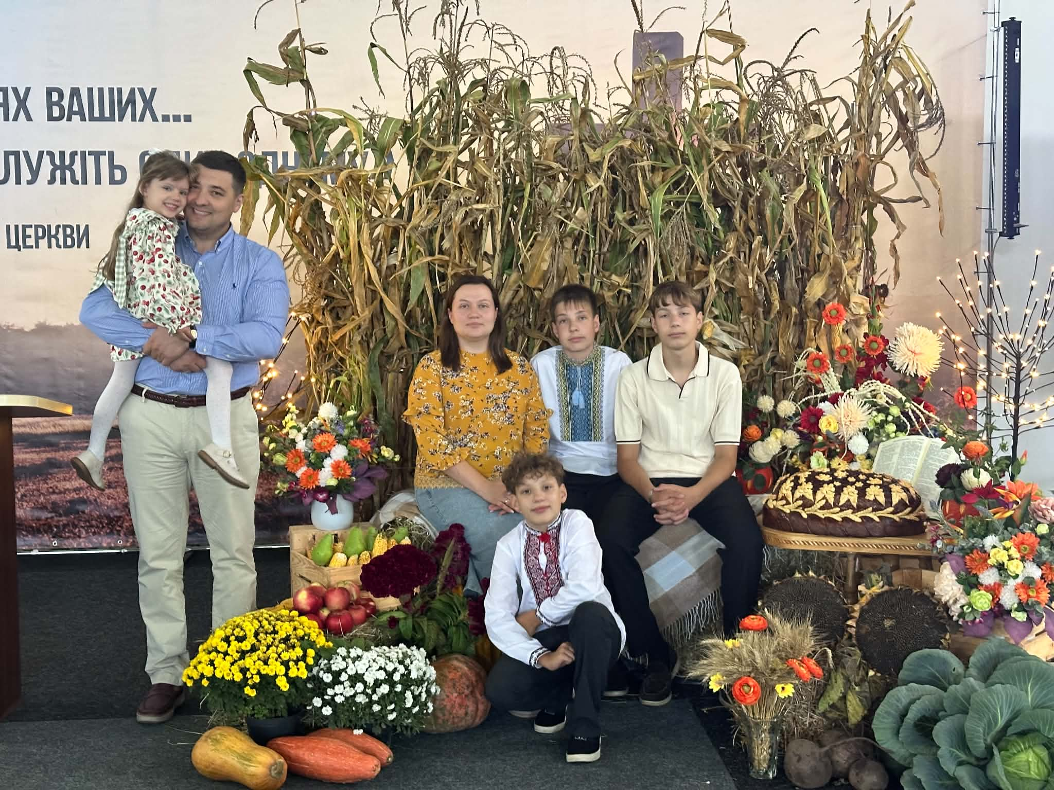 Bohdan and his family pictured together at a Harvest celebration surrounded by flowers, fruit, vegetables and crops.